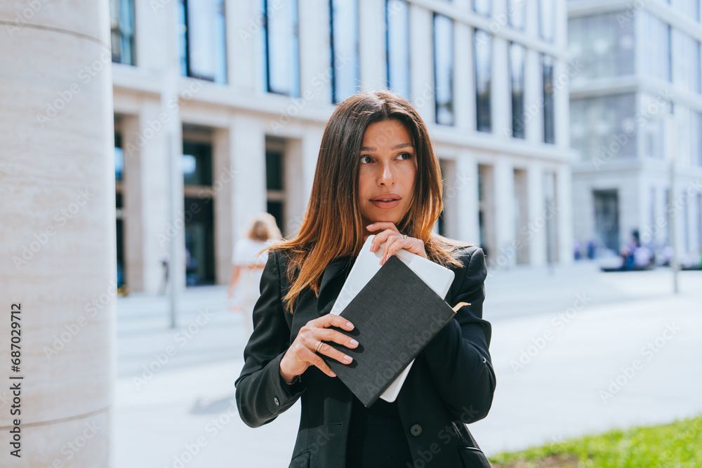 Pensive young businesswoman in black suit holds laptop, notebook looks away with thoughtful face. Discombobulated female entrepreneur makes decision, in doubts. Risk. Pensive young businesswoman in black suit holds laptop, notebook looks away with thoughtful face. Discombobulated female entrepreneur makes decision, in doubts. Risk.