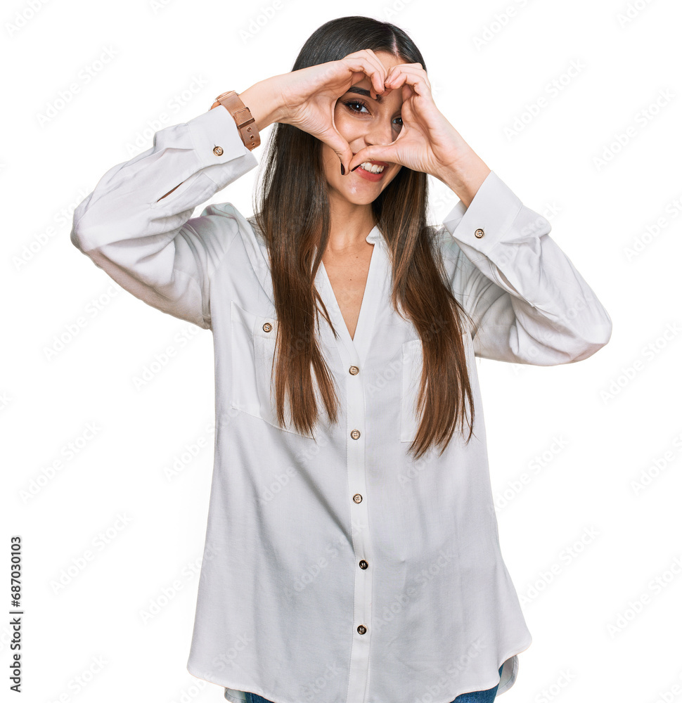 Young beautiful woman wearing casual white shirt doing heart shape with hand and fingers smiling looking through sign