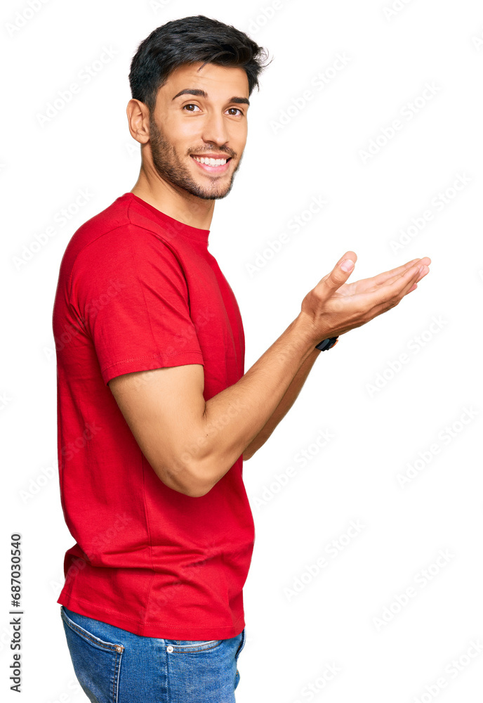 Young handsome man wearing casual red tshirt pointing aside with hands open palms showing copy space, presenting advertisement smiling excited happy Young handsome man wearing casual red tshirt pointing aside with hands open palms showing copy space, presenting advertisement smiling excited happy
