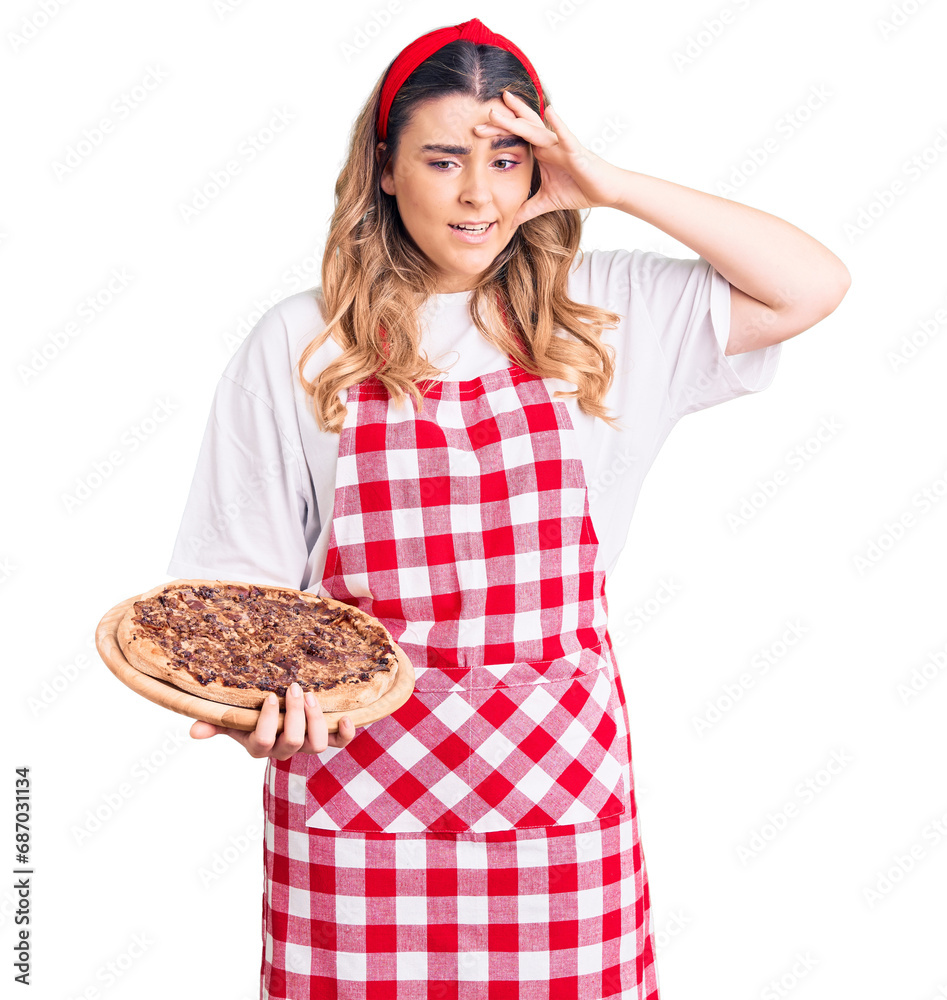 Young caucasian woman wearing apron holding pizza stressed and frustrated with hand on head, surprised and angry face Young caucasian woman wearing apron holding pizza stressed and frustrated with hand on head, surprised and angry face