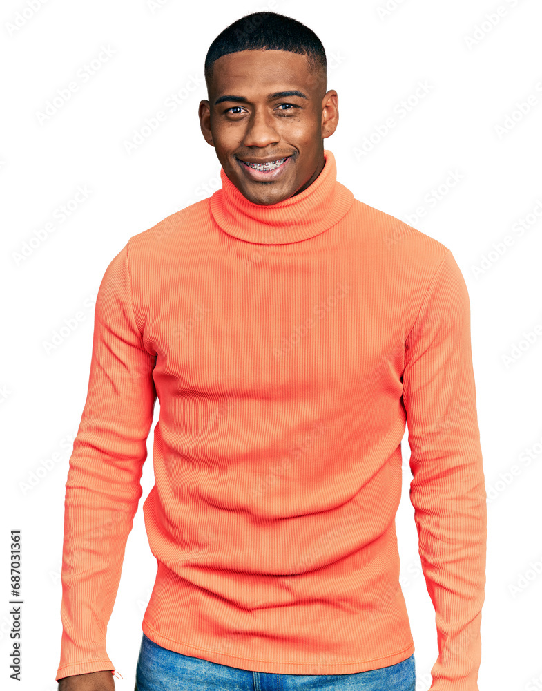Young black man wearing orange turtleneck sweater looking positive and happy standing and smiling with a confident smile showing teeth Young black man wearing orange turtleneck sweater looking positive and happy standing and smiling with a confident smile showing teeth