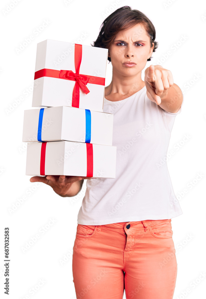 Beautiful young woman with short hair holding gifts pointing with finger to the camera and to you, confident gesture looking serious Beautiful young woman with short hair holding gifts pointing with finger to the camera and to you, confident gesture looking serious
