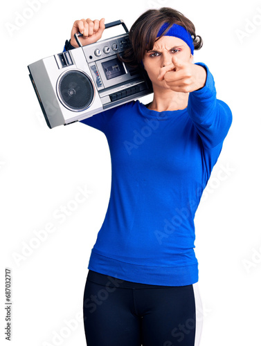 Beautiful young woman with short hair wearing workout clothes and holding boombox pointing with finger to the camera and to you, confident gesture looking serious