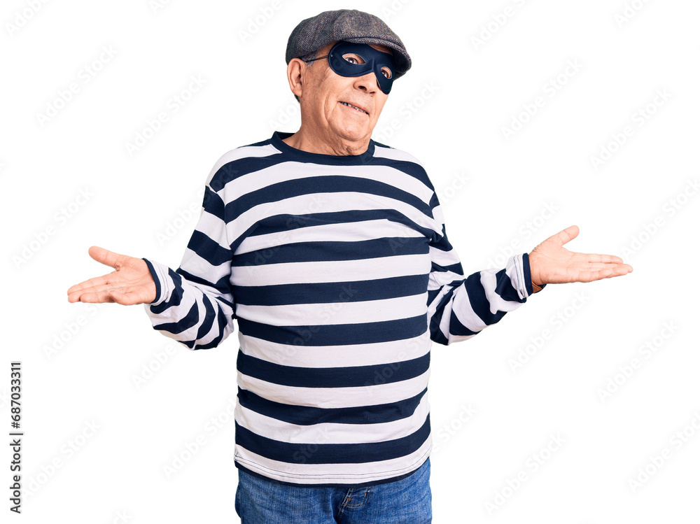 Senior handsome man wearing burglar mask and t-shirt clueless and confused expression with arms and hands raised. doubt concept. Senior handsome man wearing burglar mask and t-shirt clueless and confused expression with arms and hands raised. doubt concept.