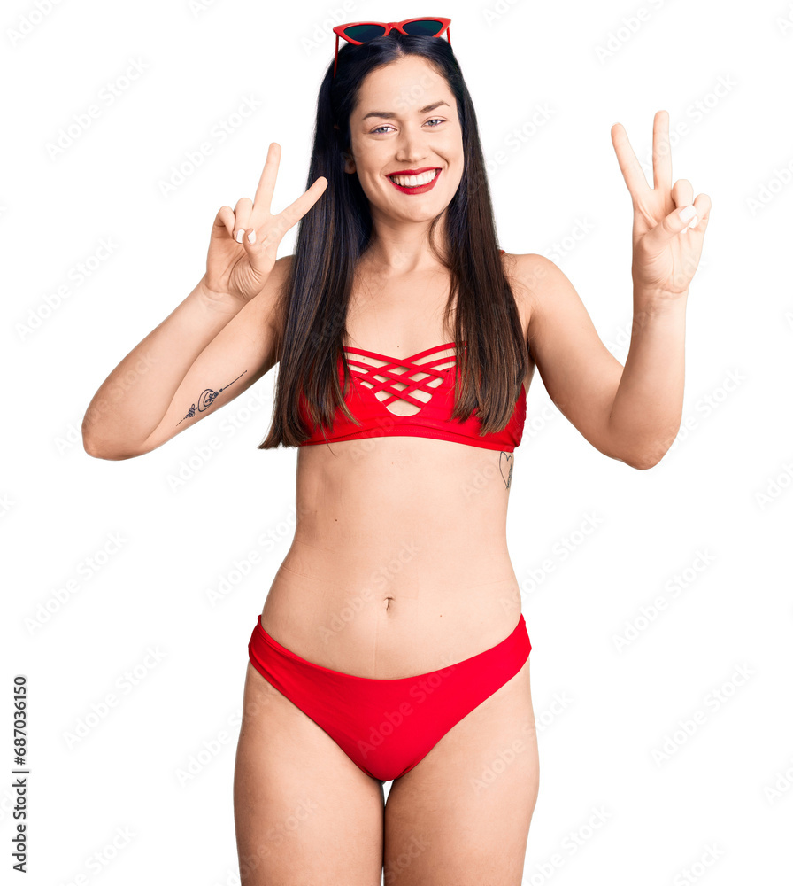 Young beautiful caucasian woman wearing bikini smiling looking to the camera showing fingers doing victory sign. number two. Young beautiful caucasian woman wearing bikini smiling looking to the camera showing fingers doing victory sign. number two.