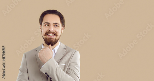 Happy successful businessman isolated on copy space banner. Studio shot of cheerful attractive young man in elegant suit thinking, smiling and looking sideways at blank beige text copyspace background