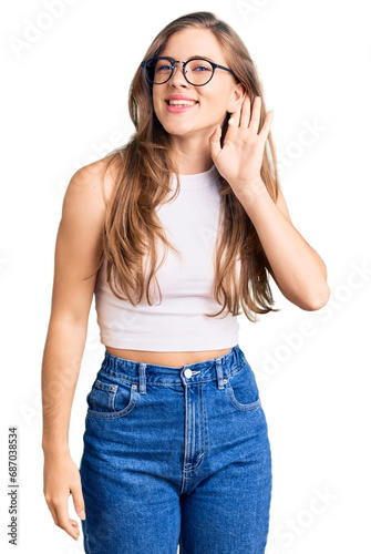 Beautiful caucasian young woman wearing casual clothes and glasses smiling with hand over ear listening an hearing to rumor or gossip. deafness concept.