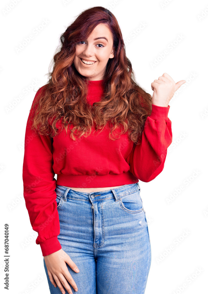 Young beautiful woman wearing casual winter sweater smiling with happy face looking and pointing to the side with thumb up. Young beautiful woman wearing casual winter sweater smiling with happy face looking and pointing to the side with thumb up.