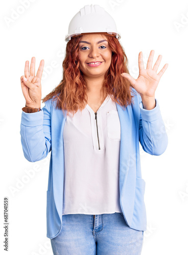 Young latin woman wearing architect hardhat showing and pointing up with fingers number eight while smiling confident and happy.