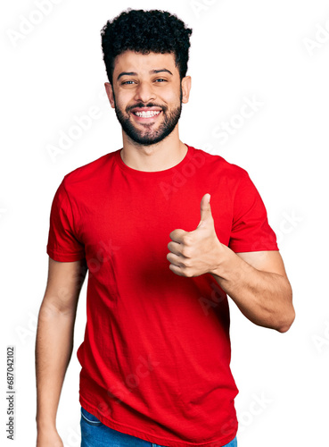 Young arab man with beard wearing casual red t shirt doing happy thumbs up gesture with hand. approving expression looking at the camera showing success.