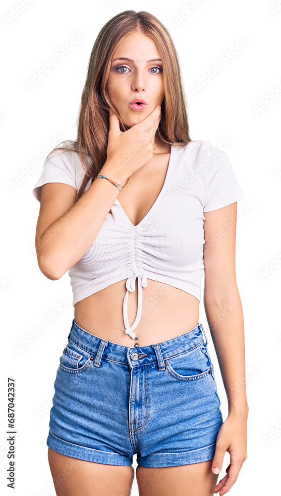 Young beautiful blonde woman wearing casual white tshirt looking fascinated with disbelief, surprise and amazed expression with hands on chin