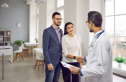 Young couple meeting in love at doctor's appointment in modern office of medical institution. Professional obstetrician gynecologist is talking to happy family, shaking hands with young woman.