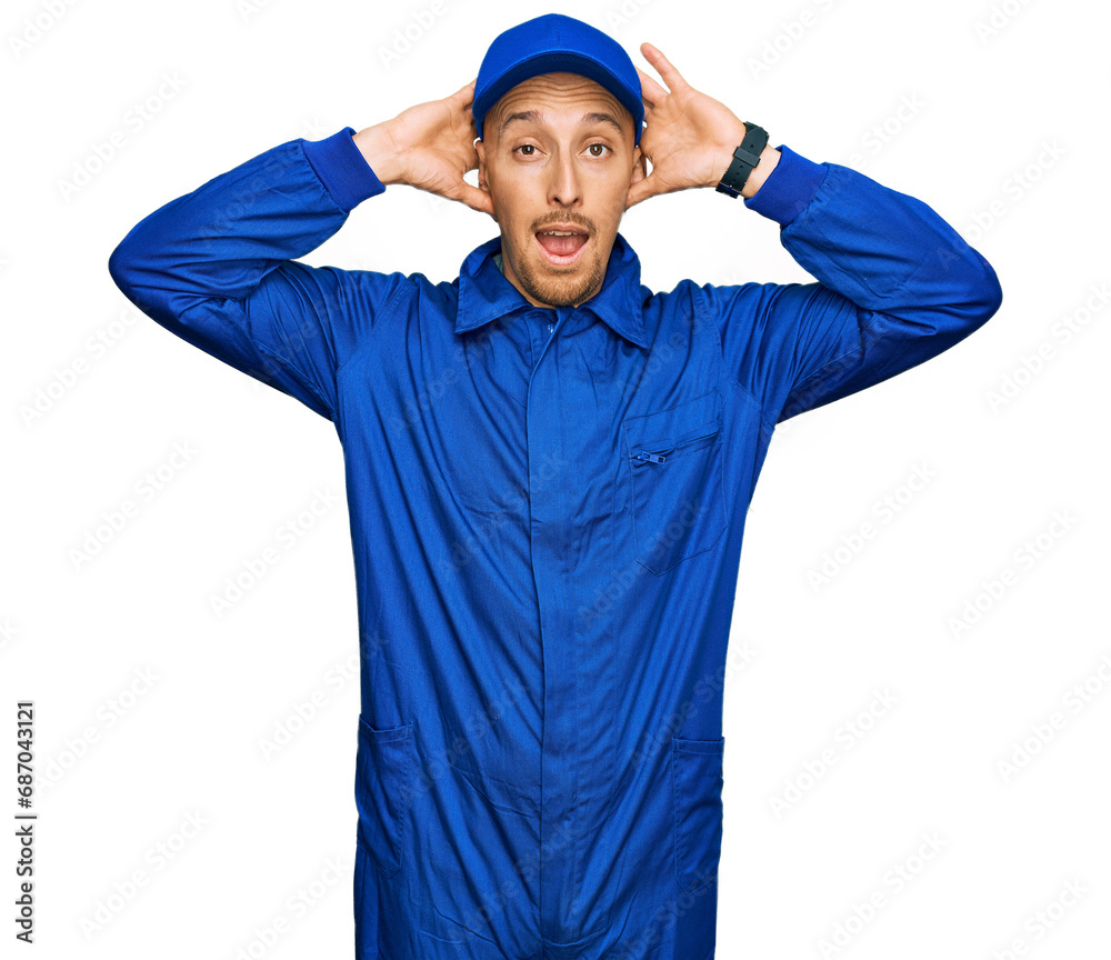 Bald man with beard wearing builder jumpsuit uniform crazy and scared with hands on head, afraid and surprised of shock with open mouth Bald man with beard wearing builder jumpsuit uniform crazy and scared with hands on head, afraid and surprised of shock with open mouth