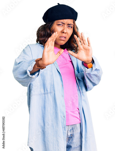 Young beautiful mixed race woman wearing french look with beret disgusted expression, displeased and fearful doing disgust face because aversion reaction. with hands raised