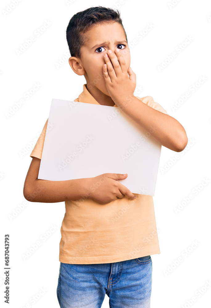 Little cute boy kid holding cardboard banner with blank space covering mouth with hand, shocked and afraid for mistake. surprised expression Little cute boy kid holding cardboard banner with blank space covering mouth with hand, shocked and afraid for mistake. surprised expression