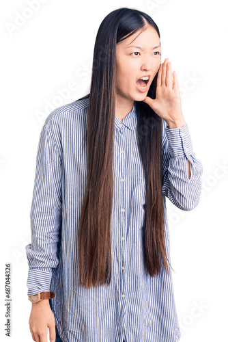 Young beautiful chinese woman wearing casual shirt shouting and screaming loud to side with hand on mouth. communication concept. © Krakenimages.com
