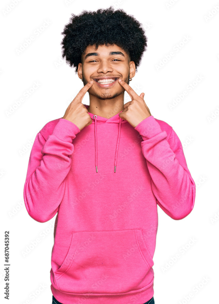 Young african american man with afro hair wearing casual pink sweatshirt smiling with open mouth, fingers pointing and forcing cheerful smile Young african american man with afro hair wearing casual pink sweatshirt smiling with open mouth, fingers pointing and forcing cheerful smile