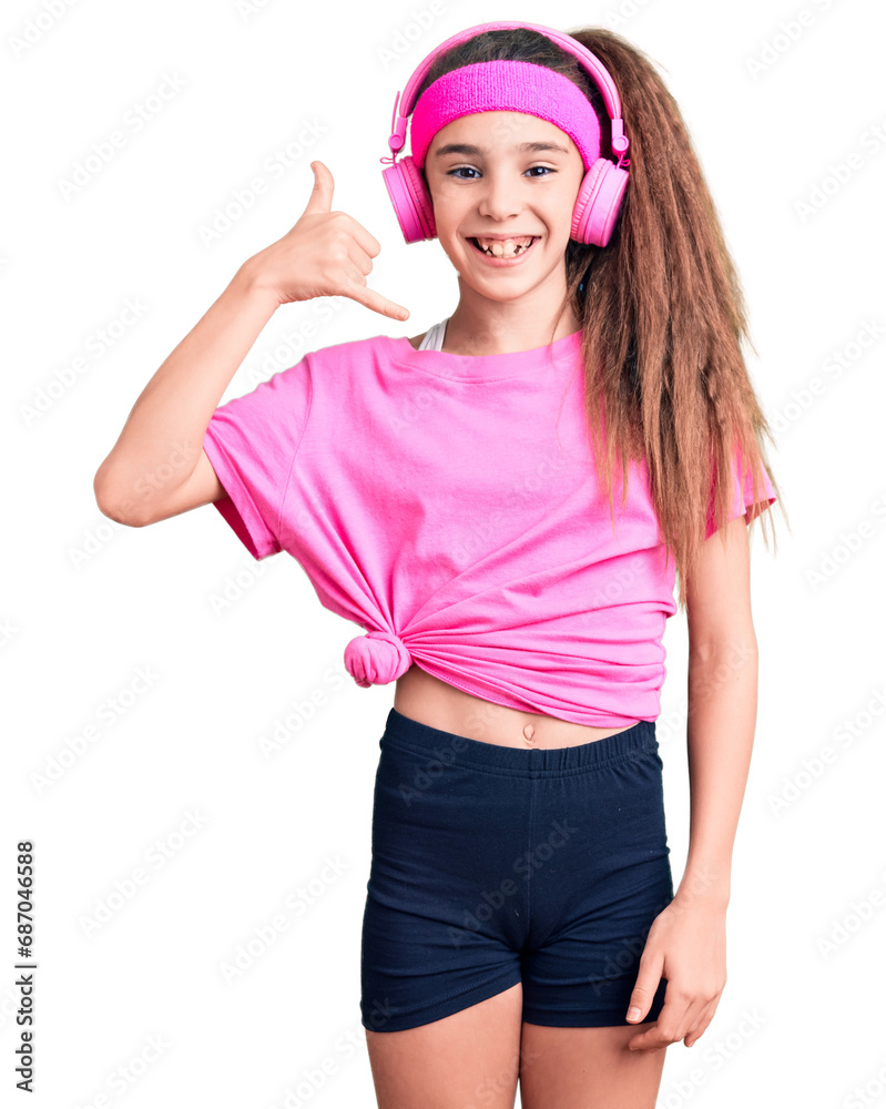 Cute hispanic child girl wearing gym clothes and using headphones smiling doing phone gesture with hand and fingers like talking on the telephone. communicating concepts. Cute hispanic child girl wearing gym clothes and using headphones smiling doing phone gesture with hand and fingers like talking on the telephone. communicating concepts.