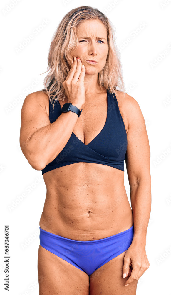 Middle age fit blonde woman wearing bikini touching mouth with hand with painful expression because of toothache or dental illness on teeth. dentist Middle age fit blonde woman wearing bikini touching mouth with hand with painful expression because of toothache or dental illness on teeth. dentist