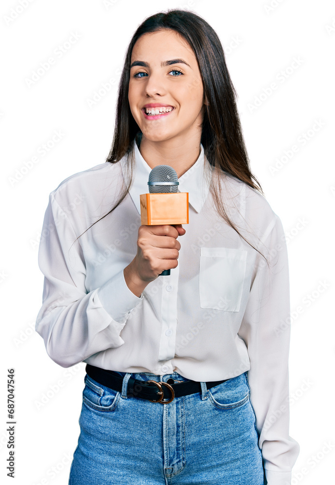 Young brunette teenager holding reporter microphone looking positive and happy standing and smiling with a confident smile showing teeth Young brunette teenager holding reporter microphone looking positive and happy standing and smiling with a confident smile showing teeth