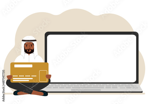 A man sits cross-legged and holds a large plastic card. Next to the man is a large laptop with space for text.