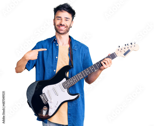Young hispanic man playing electric guitar pointing finger to one self smiling happy and proud photo