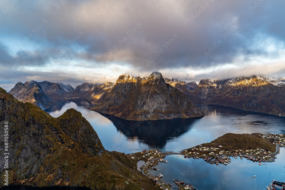 view from Reinebringen mountain over reine village with mountains reflected in water with golden color on lofoten islands in norway