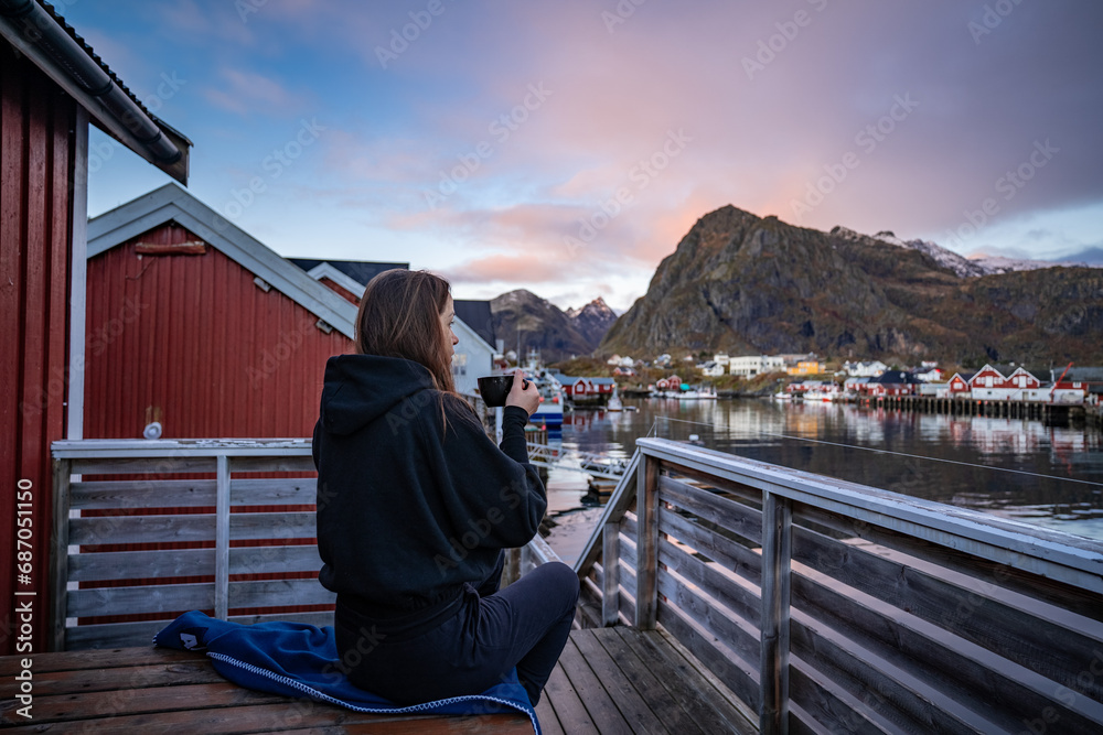 Morning Coffee by the Bay: Woman Enjoying Sørvågen Fisherman Village with Red Houses, Lofoten Islands, Norway