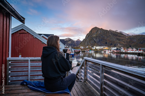 Obraz na płótnie Morning Coffee by the Bay: Woman Enjoying Sørvågen Fisherman Village with Red Houses, Lofoten Islands, Norway w salonie