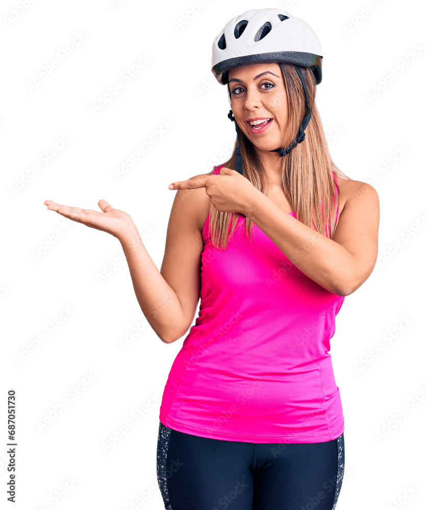 Young beautiful woman wearing bike helmet amazed and smiling to the camera while presenting with hand and pointing with finger. Young beautiful woman wearing bike helmet amazed and smiling to the camera while presenting with hand and pointing with finger.