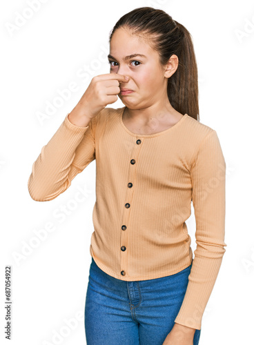 Beautiful brunette little girl wearing casual sweater smelling something stinky and disgusting, intolerable smell, holding breath with fingers on nose. bad smell