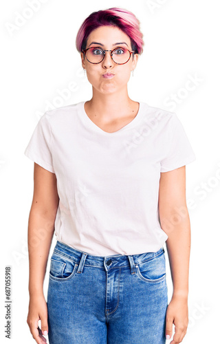 Young beautiful woman with pink hair wearing casual clothes and glasses puffing cheeks with funny face. mouth inflated with air, crazy expression. © Krakenimages.com
