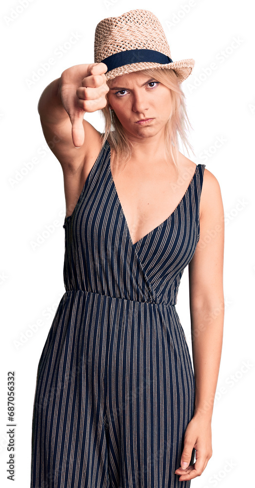 Young beautiful blonde woman wearing summer hat and dress looking unhappy and angry showing rejection and negative with thumbs down gesture. bad expression. Young beautiful blonde woman wearing summer hat and dress looking unhappy and angry showing rejection and negative with thumbs down gesture. bad expression.