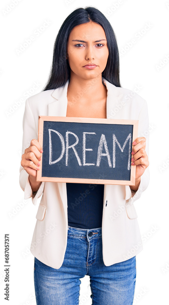 Young beautiful latin girl holding blackboard with dream word thinking attitude and sober expression looking self confident Young beautiful latin girl holding blackboard with dream word thinking attitude and sober expression looking self confident
