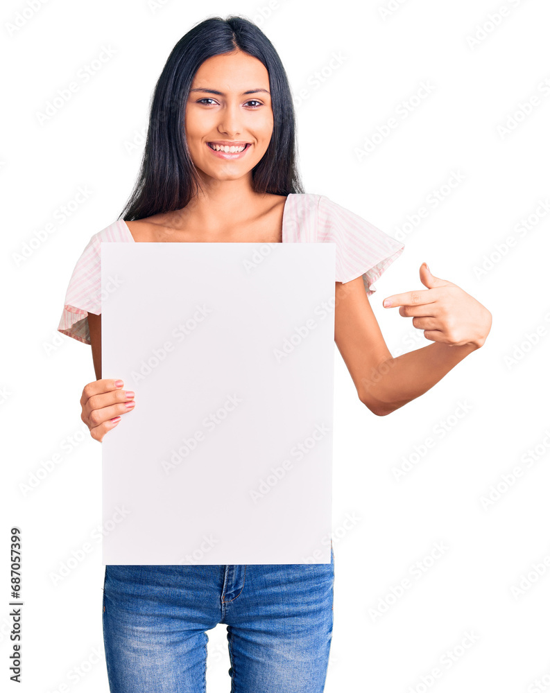 Young beautiful latin girl holding blank empty banner smiling happy pointing with hand and finger Young beautiful latin girl holding blank empty banner smiling happy pointing with hand and finger