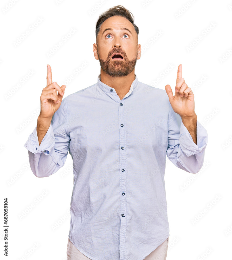 Handsome middle age man wearing business shirt amazed and surprised looking up and pointing with fingers and raised arms. Handsome middle age man wearing business shirt amazed and surprised looking up and pointing with fingers and raised arms.