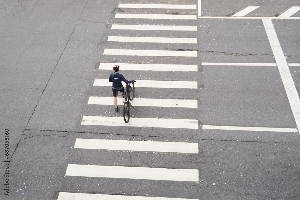 © nuclear_lily - Man crosses the road at a pedestrian crossing and carries a bicycle next to him. View from above.