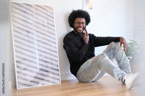 Black and afro man sitting on the floor of his office next to a large poster. He is laughing out loud during a phone call. Fun time during work photo