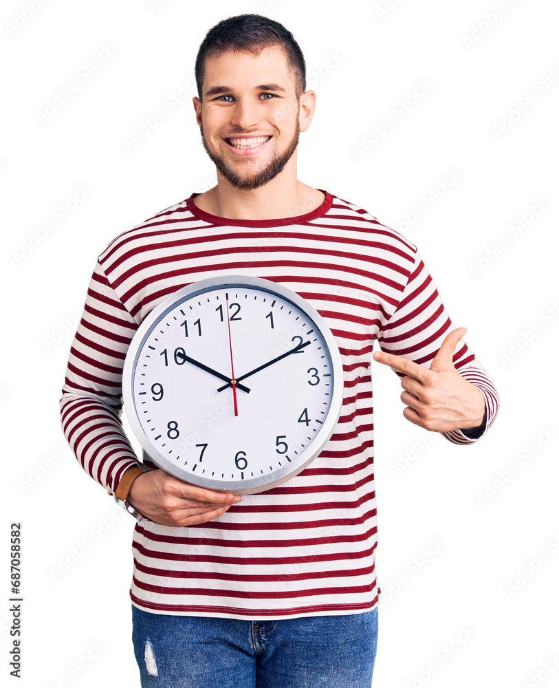 Young handsome man holding big clock smiling happy pointing with hand and finger Young handsome man holding big clock smiling happy pointing with hand and finger