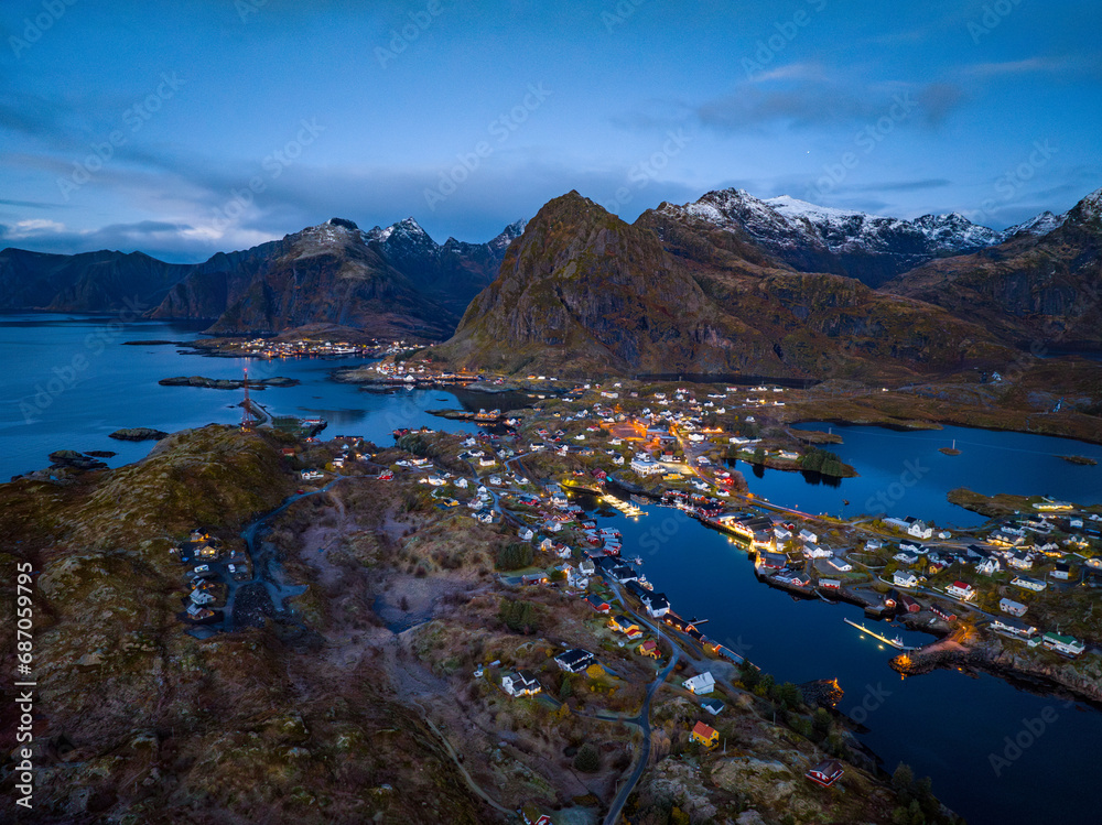 aerial view over early morning fisherman Sørvågen village bay with switched on street lights with mountains on background on lofoten islands, norway