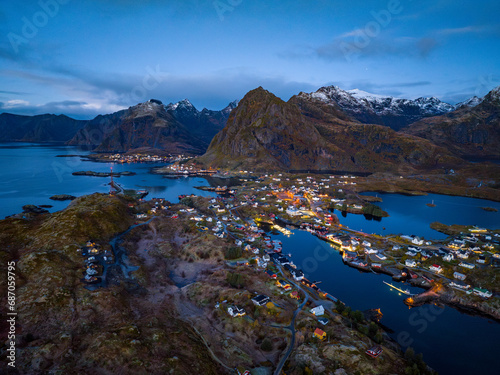 Obraz na płótnie aerial view over early morning fisherman Sørvågen village bay with switched on street lights with mountains on background on lofoten islands, norway w salonie