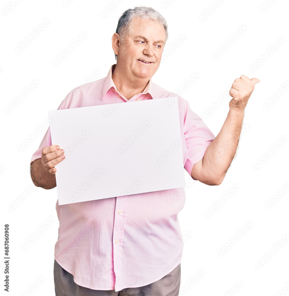 Senior grey-haired man holding blank empty banner pointing thumb up to the side smiling happy with open mouth Senior grey-haired man holding blank empty banner pointing thumb up to the side smiling happy with open mouth