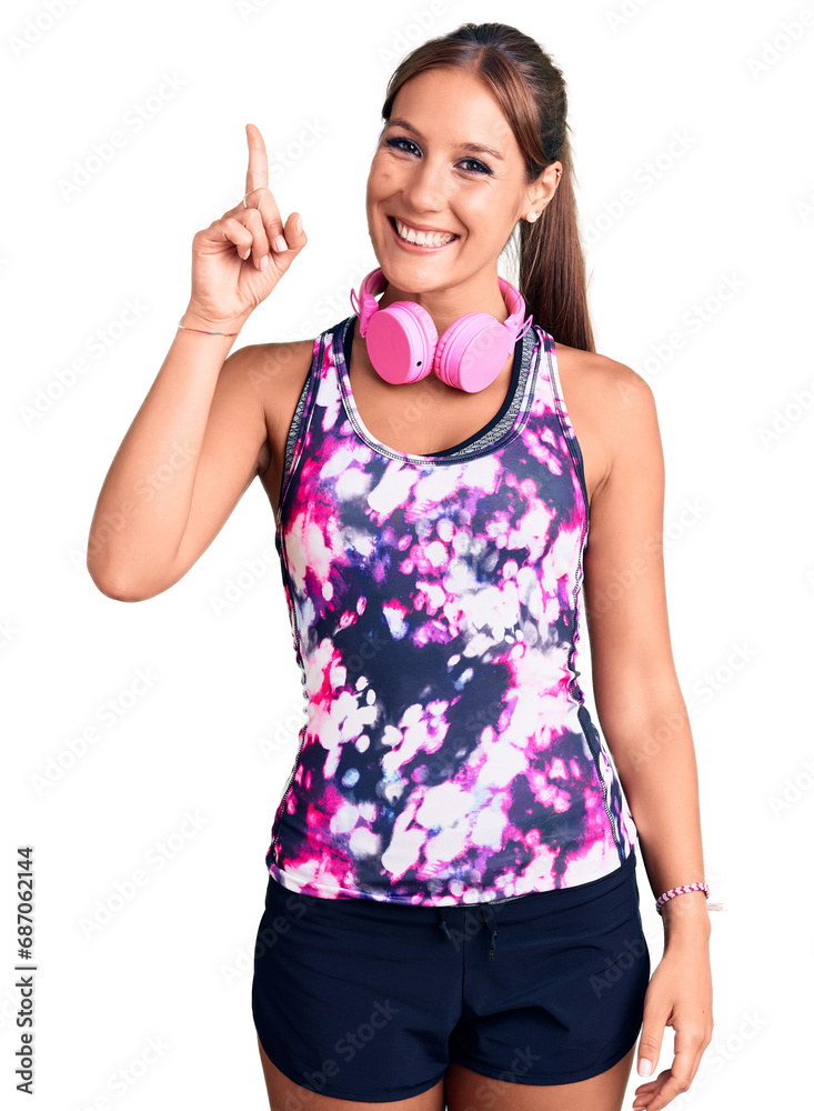 Young beautiful hispanic woman wearing gym clothes and using headphones pointing finger up with successful idea. exited and happy. number one. Young beautiful hispanic woman wearing gym clothes and using headphones pointing finger up with successful idea. exited and happy. number one.