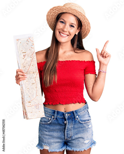 Young beautiful hispanic woman wearing summer hat holding city map surprised with an idea or question pointing finger with happy face, number one