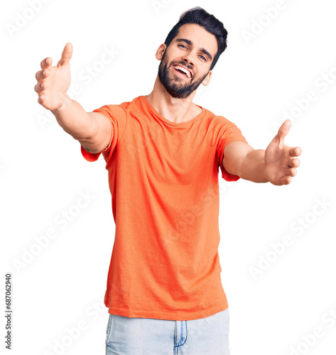 Young handsome man with beard wearing casual t-shirt looking at the camera smiling with open arms for hug. cheerful expression embracing happiness.