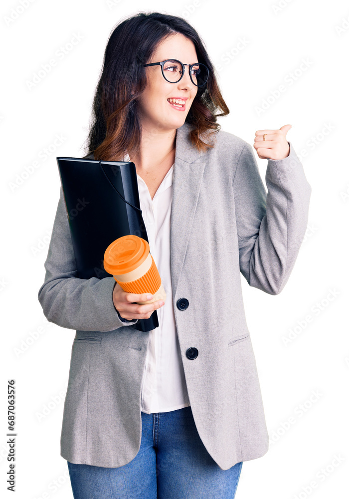 Beautiful young brunette woman holding business folder and drinking coffee pointing thumb up to the side smiling happy with open mouth Beautiful young brunette woman holding business folder and drinking coffee pointing thumb up to the side smiling happy with open mouth