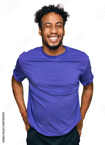 Young african american man with beard wearing casual purple t shirt winking looking at the camera with sexy expression, cheerful and happy face.