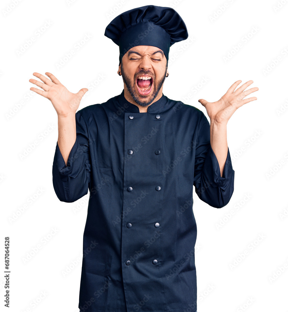 Young hispanic man wearing cooker uniform celebrating mad and crazy for success with arms raised and closed eyes screaming excited. winner concept Young hispanic man wearing cooker uniform celebrating mad and crazy for success with arms raised and closed eyes screaming excited. winner concept