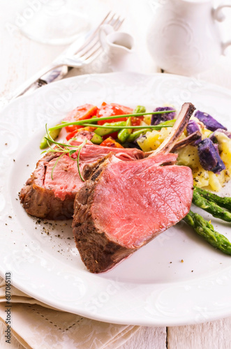 Traditional barbecue carree of venison with potato salad and green asparagus served as close-up on a classic design plate