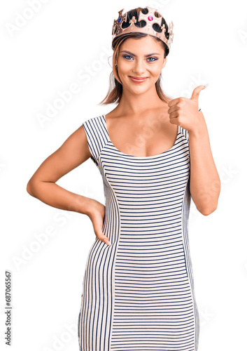 Young beautiful woman wearing king crown smiling happy and positive, thumb up doing excellent and approval sign